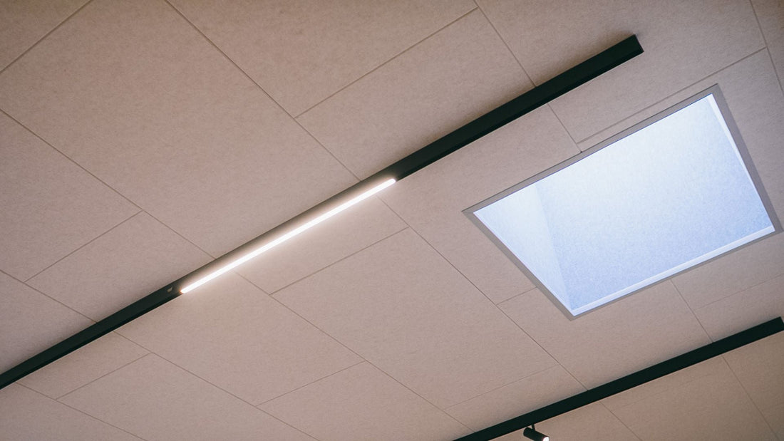 Akustikpaneler monteret direkte på eksisterende loft med integreret belysning og ovenlys set nedefra